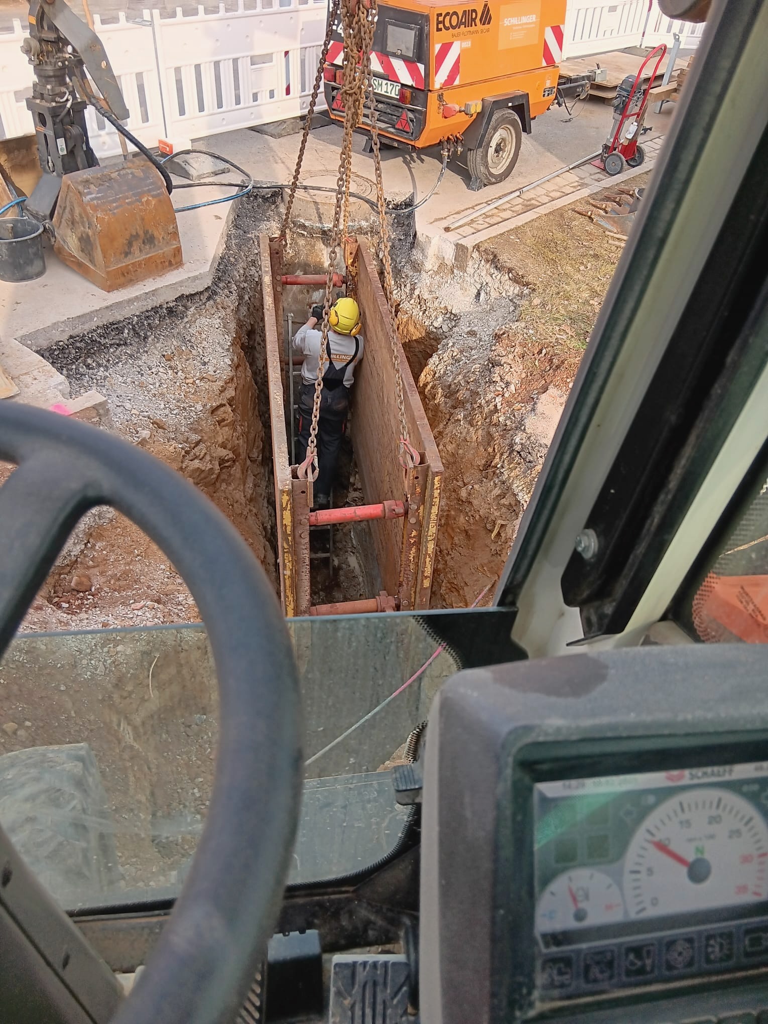 Baustelle im Tief- und Kanalbau, bei der ein Arbeiter in einem gesicherten Graben mit Verbau arbeitet