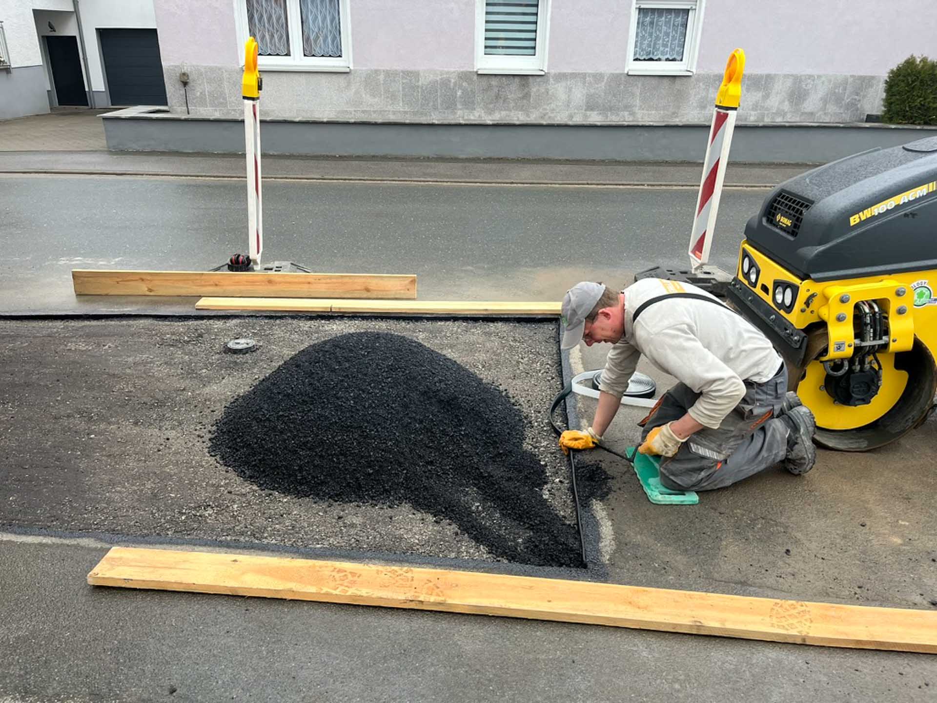 Ein Mitarbeiter von Schillinger kniet vor Asphaltwalze und teert Straßenabschnitt neu